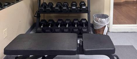 A gym with a bench, dumbbells, and a basket.