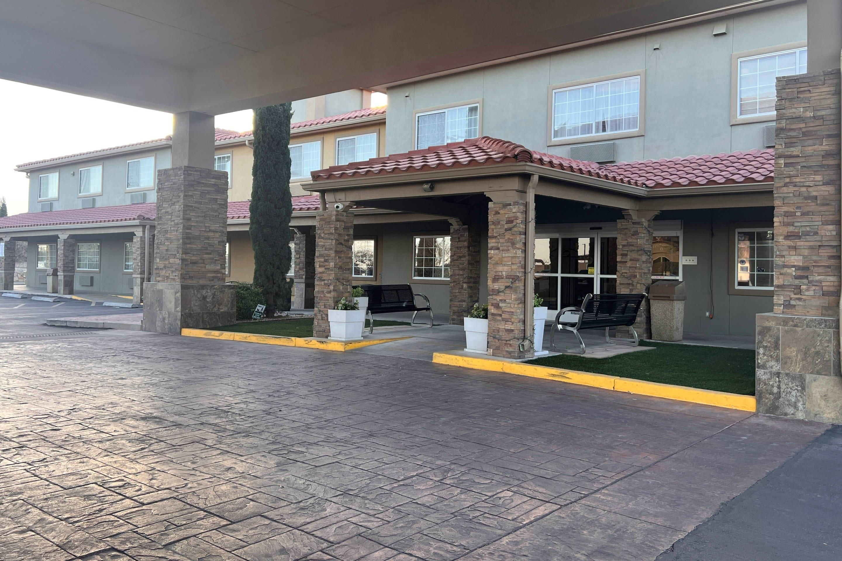A hotel entrance with a covered patio, stone pillars, and a tiled roof.