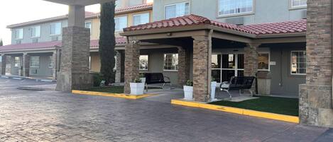 A hotel entrance with a covered patio, stone pillars, and a tiled roof.