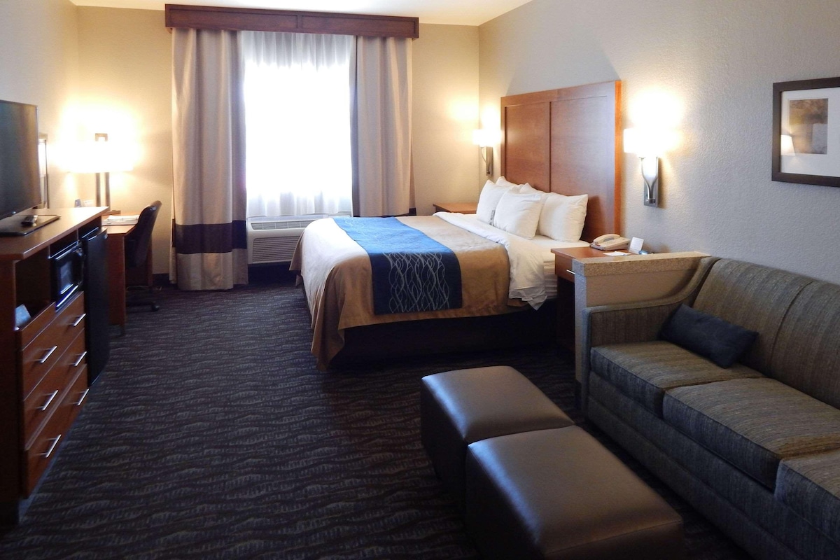 A hotel room with a bed, a desk, a chair, a sofa, and a TV.