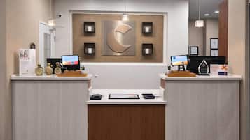 A reception desk with two computer monitors, a large wall-mounted logo, and a wooden reception desk.