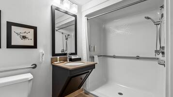 Une salle de bain moderne comprenant des toilettes, un lavabo, un miroir, une douche et un tableau encadré accroché au mur.