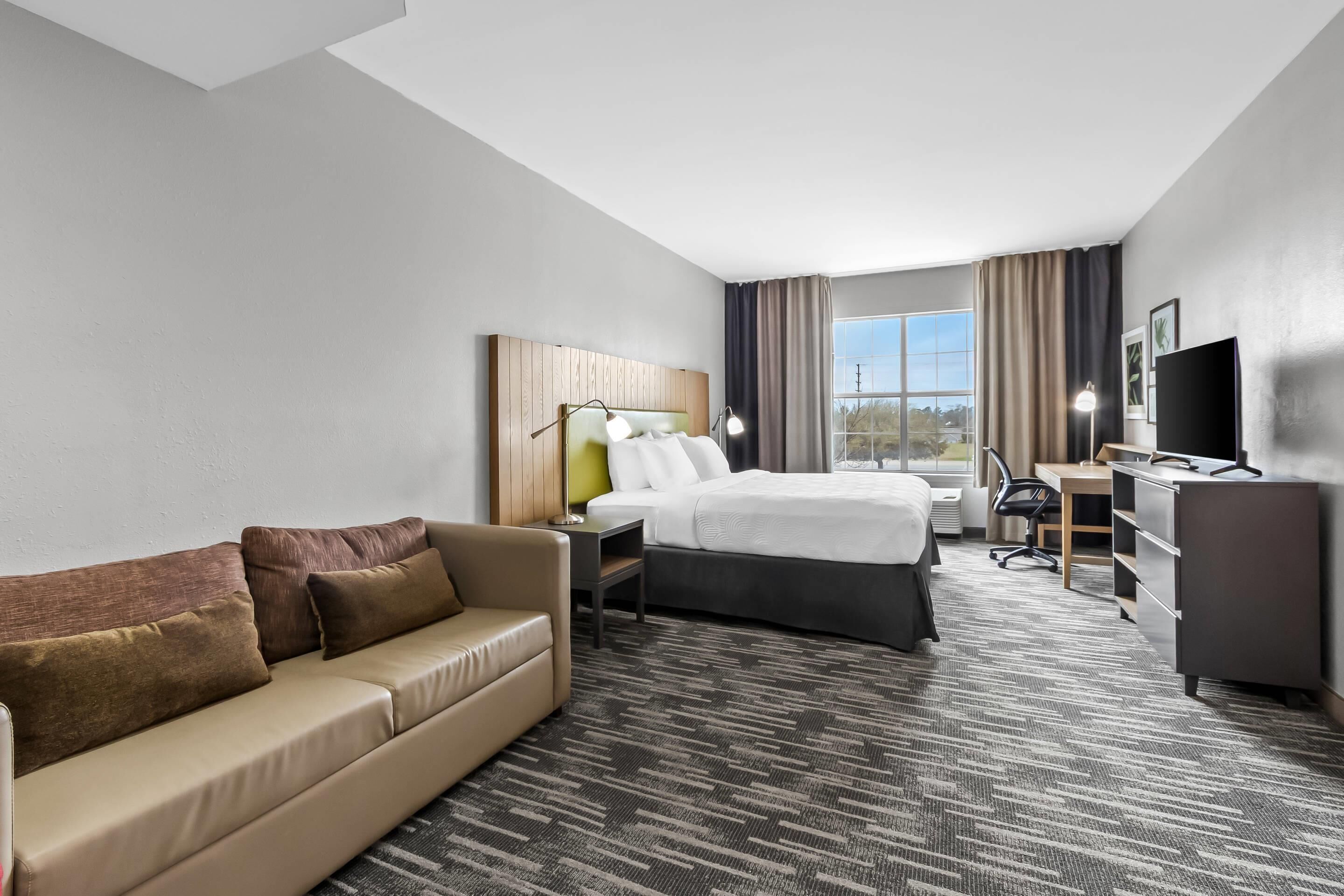A hotel room with a bed, a sofa, a desk, a TV, and a window with curtains.