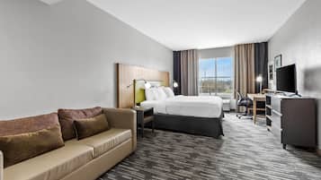 A hotel room with a bed, a sofa, a desk, a TV, and a window with curtains.
