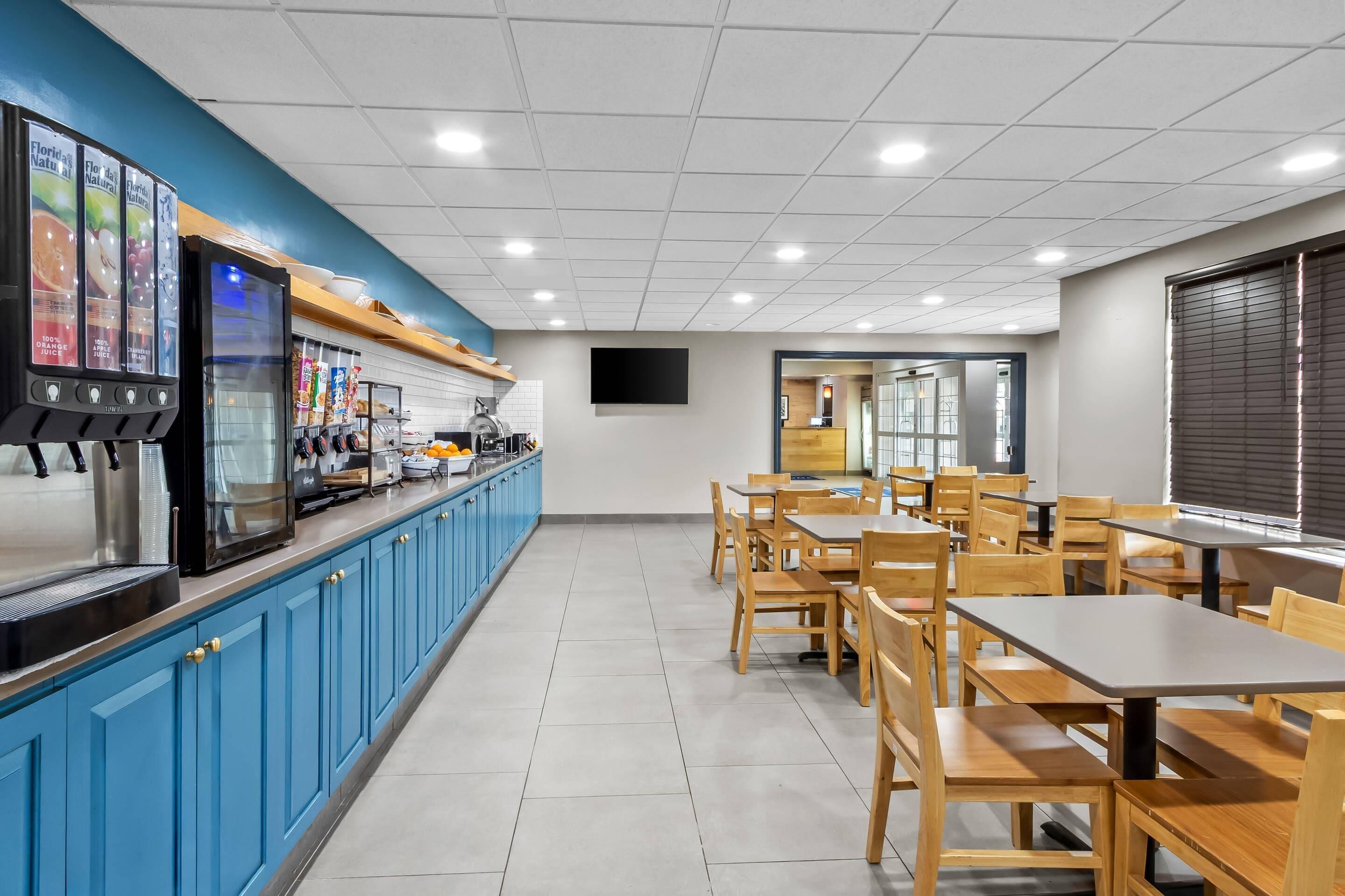 A clean, well-lit cafeteria with blue cabinets, stainless steel appliances, and wooden tables and chairs.