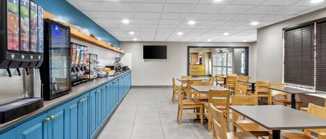 A clean, well-lit cafeteria with blue cabinets, stainless steel appliances, and wooden tables and chairs.