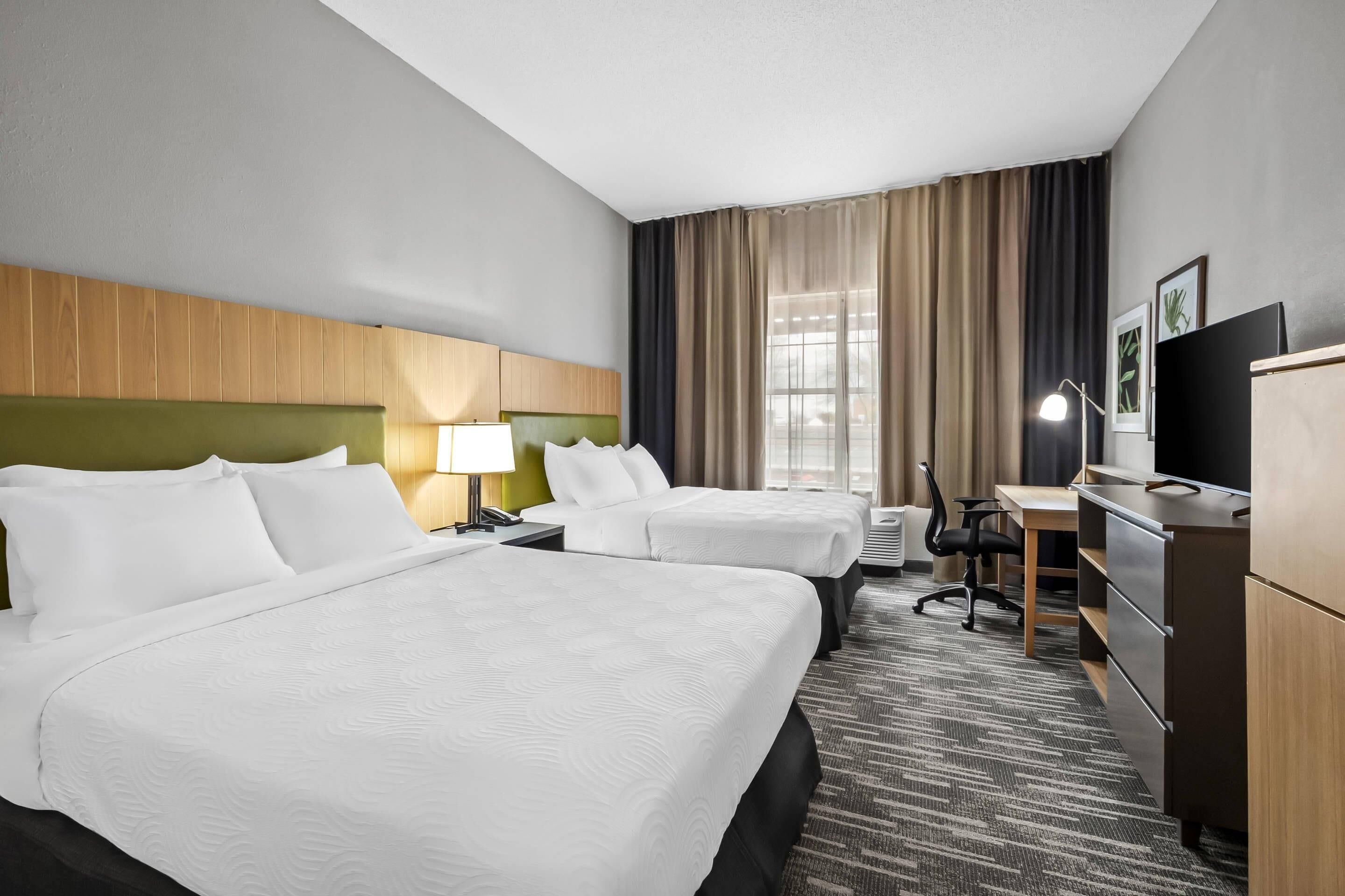 A hotel room with two beds, a desk, a chair, a TV, and a window with curtains.