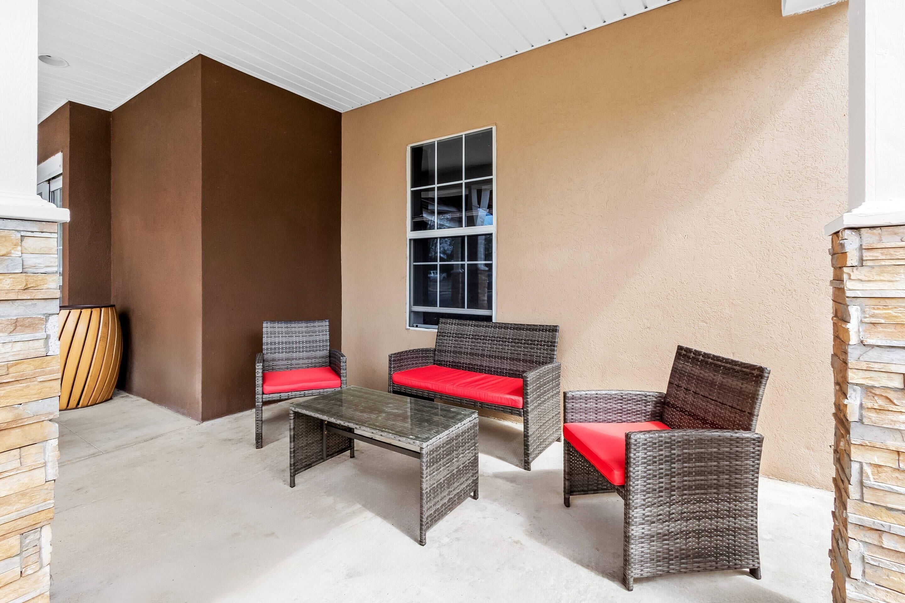 Un patio amoblado con mobiliario de mimbre, una mesa de vidrio y un muro decorativo de piedra.