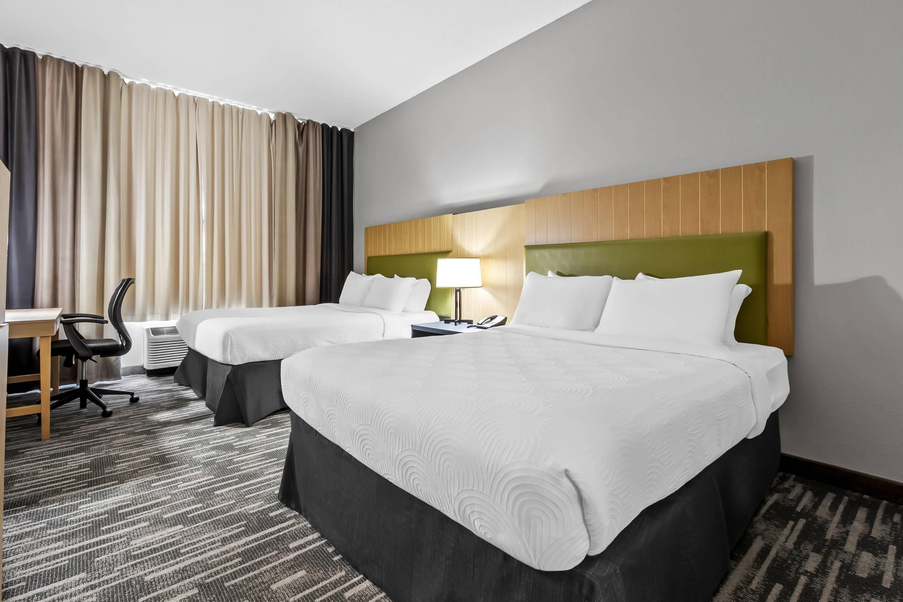 A hotel room with two beds, a desk, a chair, a lamp, and a window with curtains.