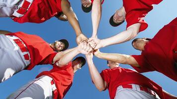 A group of people in red and white sports uniforms forming a circle with their hands together.