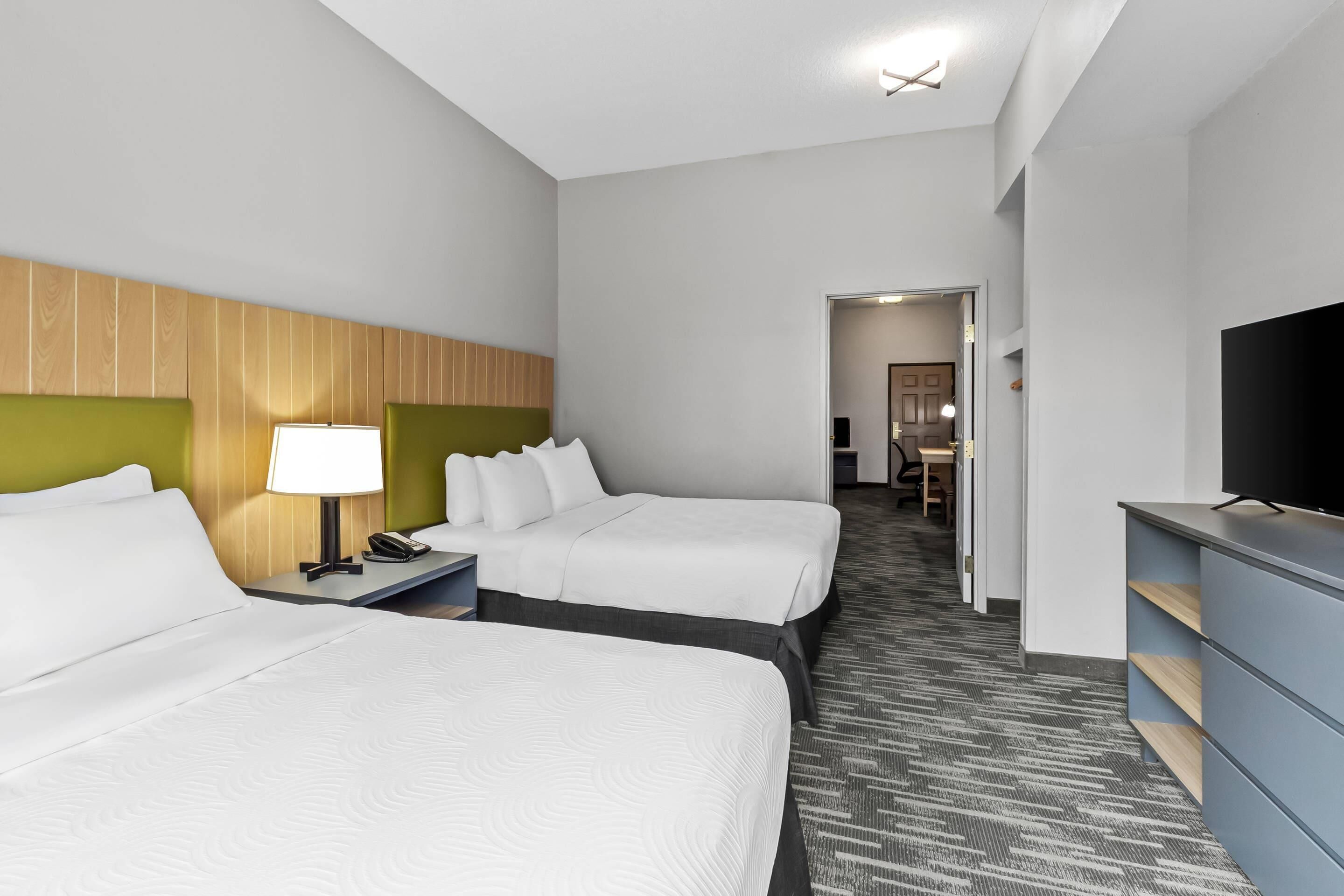 A hotel room with two beds, a desk with a lamp, a television, and a carpeted floor.
