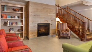 Un vaste espace de vie agrémenté d’une cheminée, d’un escalier en bois et d’une bibliothèque remplie de livres.