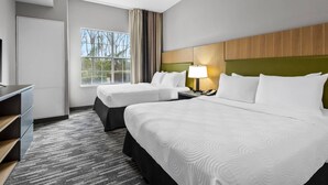 Une chambre d’hôtel avec deux lits, un bureau, une chaise, une lampe et une fenêtre donnant sur des arbres.