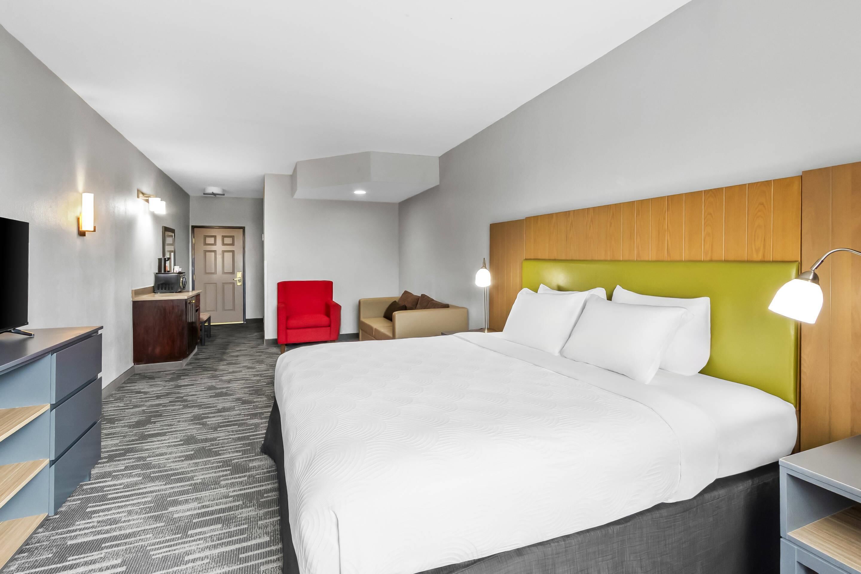 A hotel room with a bed, a desk, a chair, a TV, and a door.