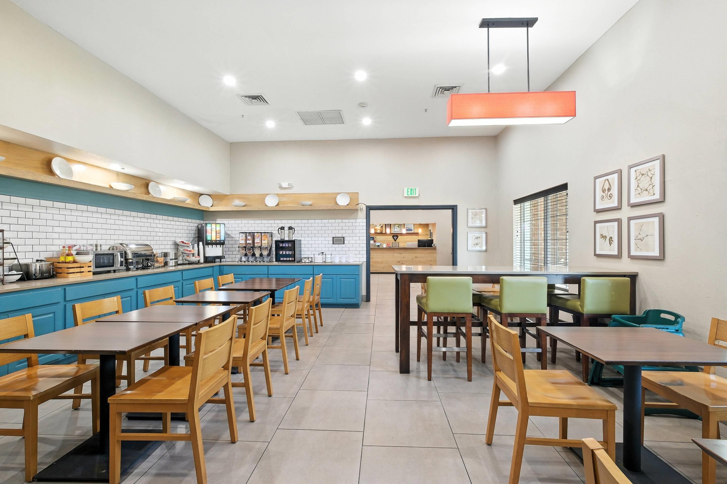Un restaurante moderno con una decoración azul y blanca, que presenta una larga barra con una máquina de café, un área de comedor con mesas y sillas de madera, y obras de arte enmarcadas en las paredes.