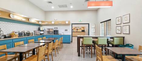 Un restaurante moderno con una decoración azul y blanca, que presenta una larga barra con una máquina de café, un área de comedor con mesas y sillas de madera, y obras de arte enmarcadas en las paredes.