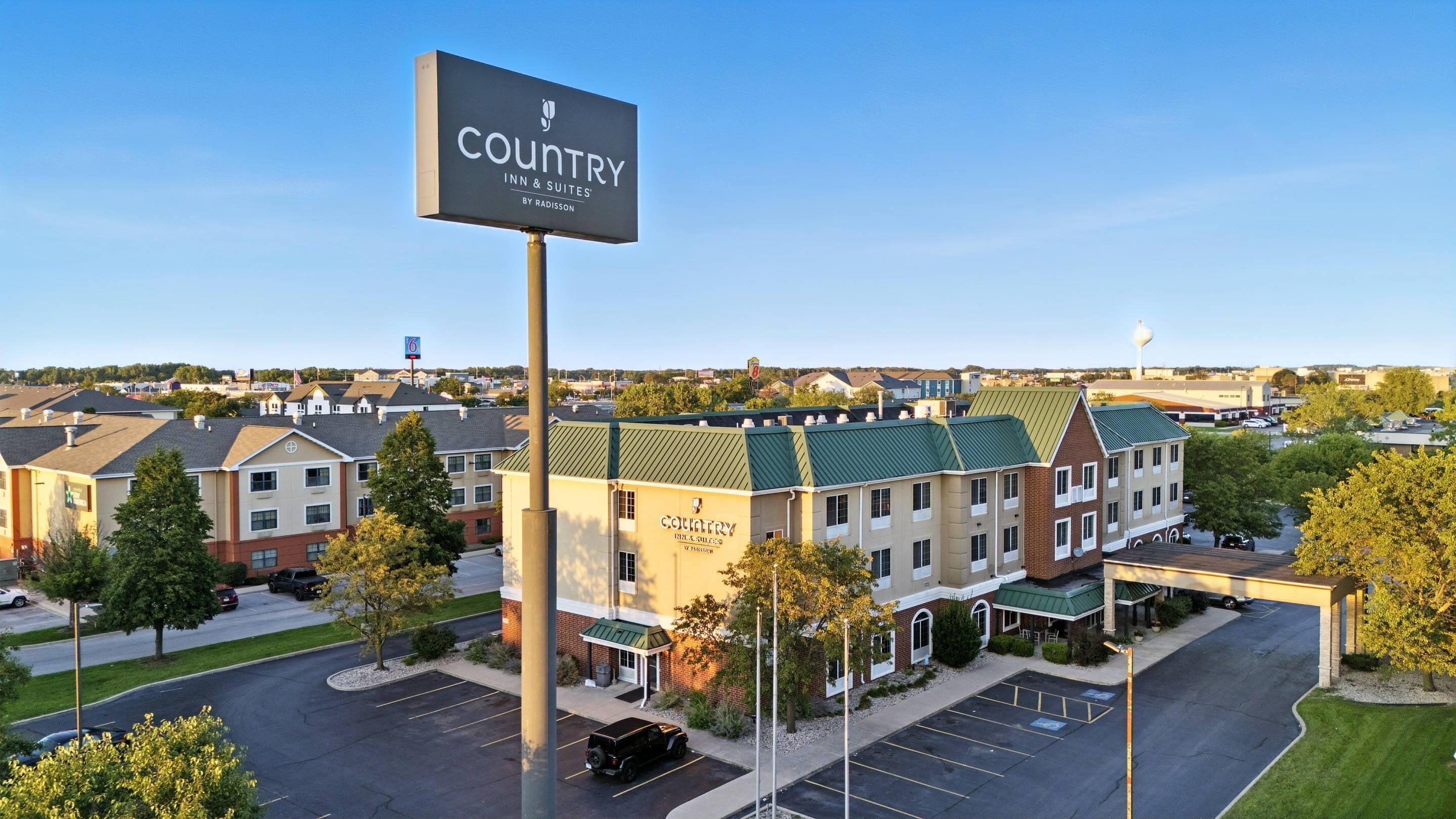 A hotel with a Country Inn & Suites sign, multiple buildings, parking, and a clear sky.