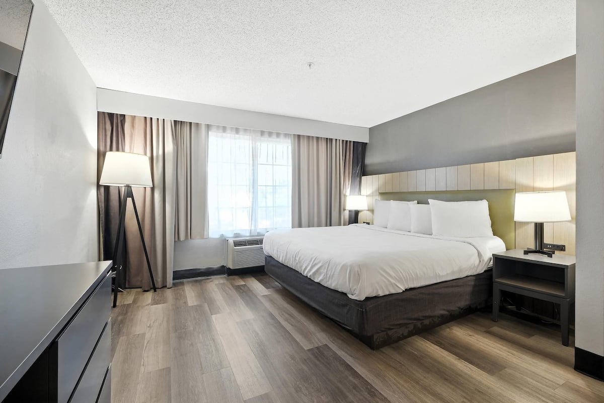 A modern hotel room with a large bed, bedside lamps, a desk, and a window with curtains.