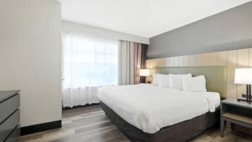 Una habitación de hotel con una cama grande, mesitas de noche, un aparador y una ventana con cortinas.