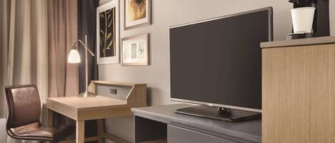 A hotel room with a desk, chair, television, and a coffee machine.