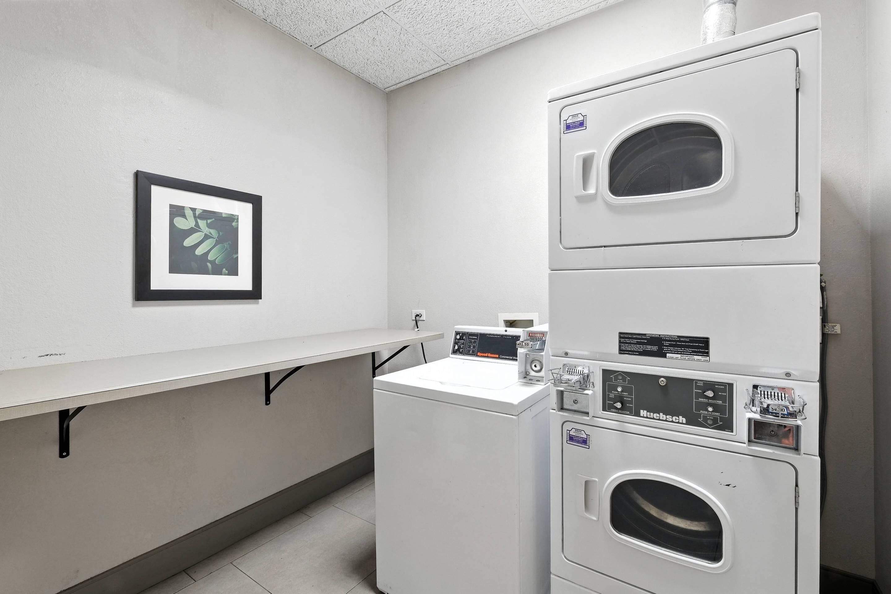 A laundry room with stacked washers and dryers, a white countertop, and a framed picture on the wall.
