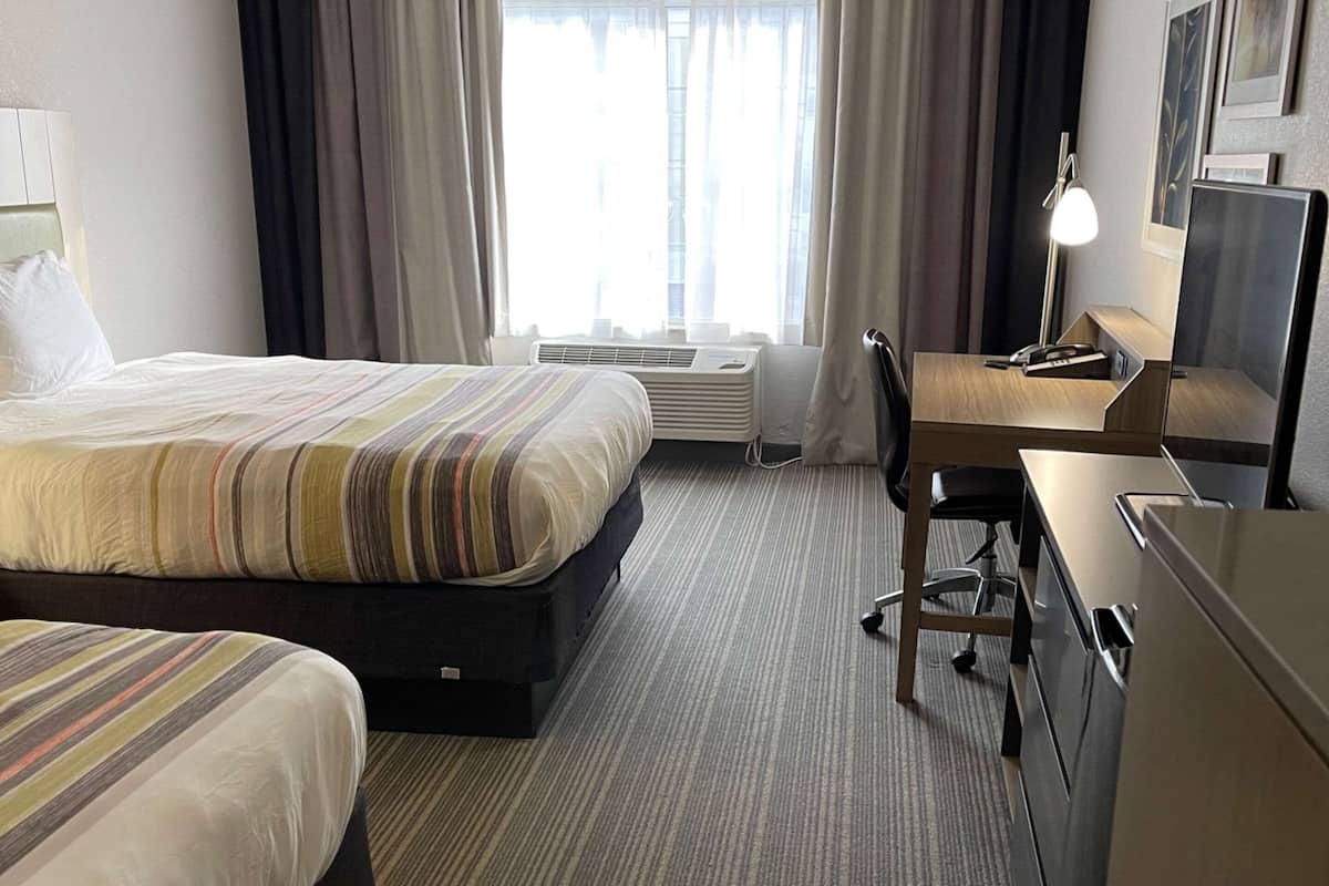 A hotel room with a bed, a desk, a chair, a desk lamp, and a wardrobe.