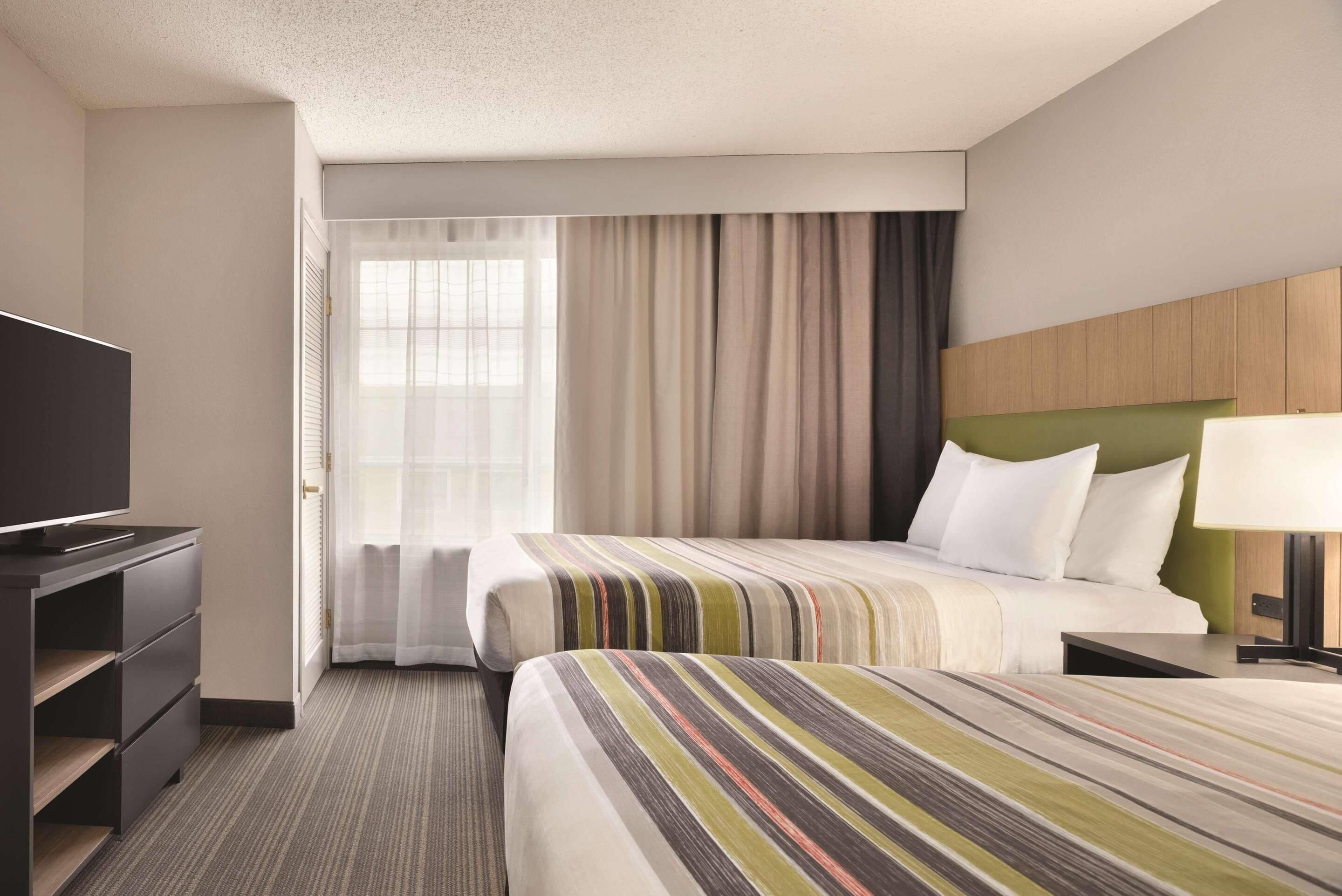 Ein Hotelzimmer mit Bett, Fernseher, Schreibtisch und einem Fenster mit Vorhängen.