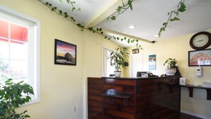 A reception area with a wooden reception desk, a clock, and a plant. - Morro Bay Beach Inn (Morro Bay)