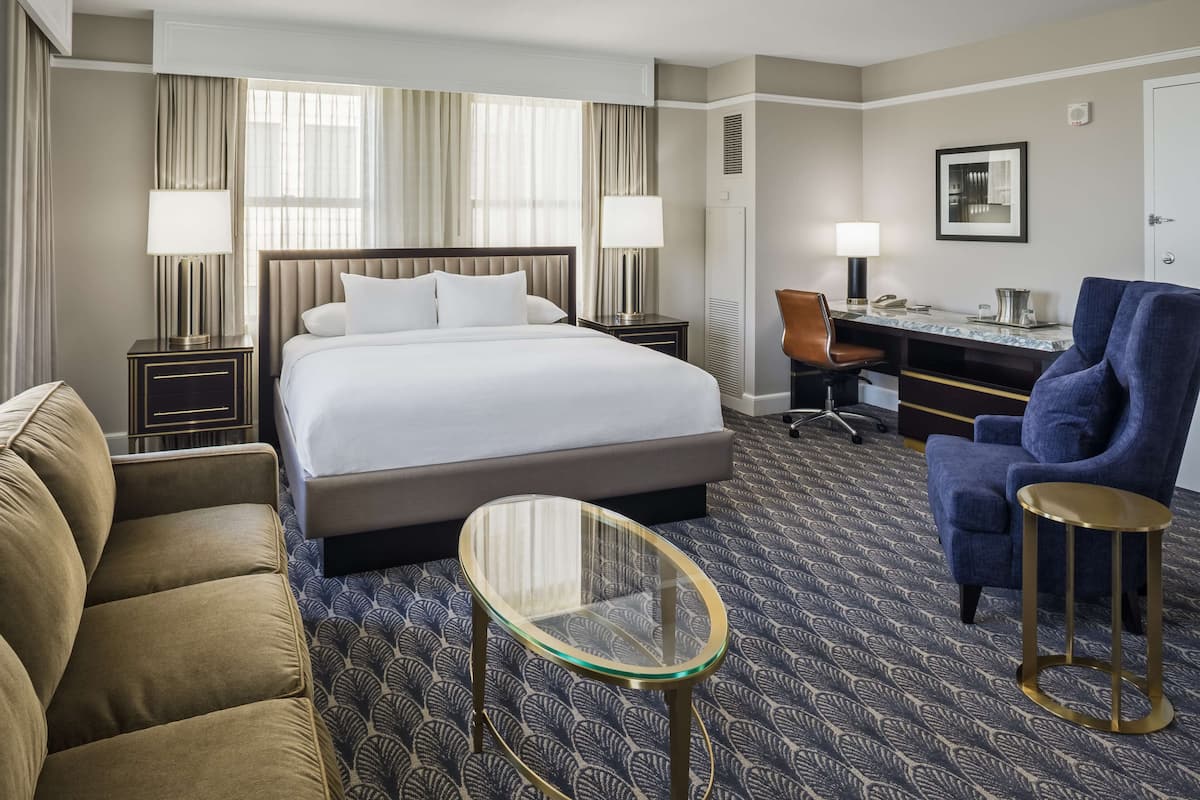 A hotel room with a large bed, a desk, a chair, and a small table.