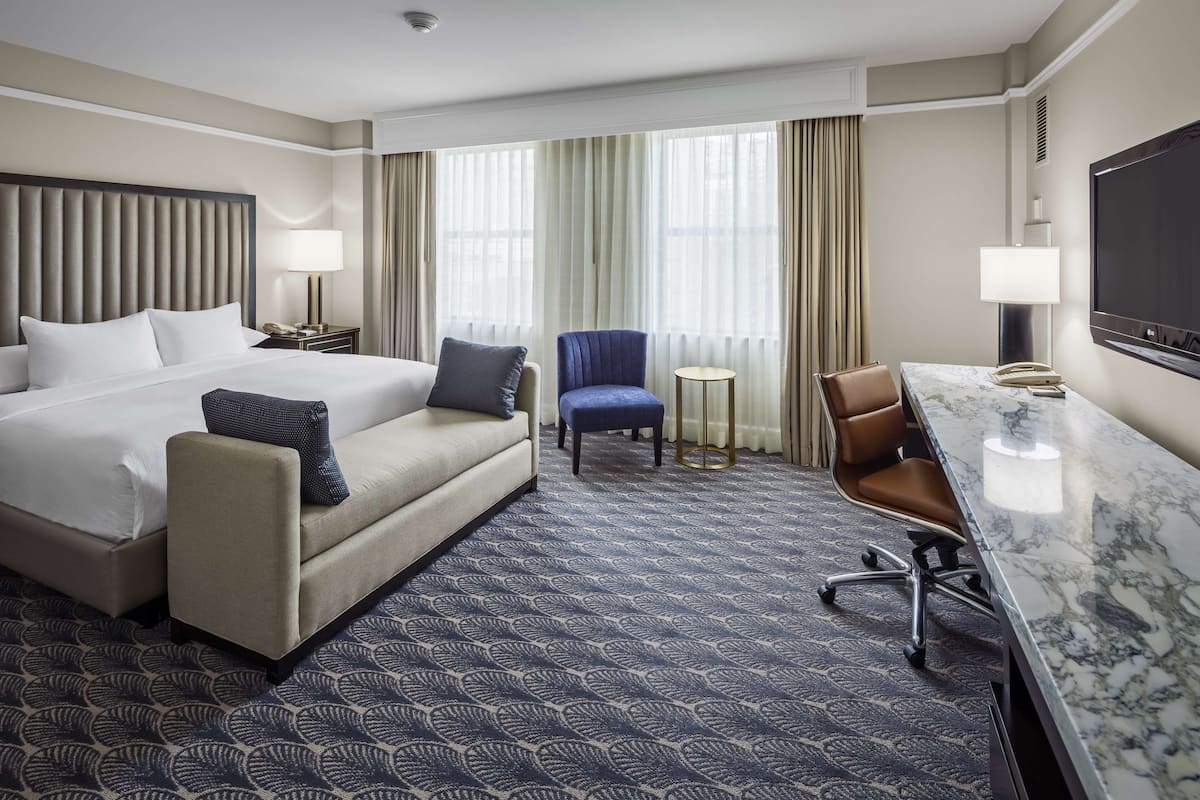 A hotel room with a large bed, a sofa, a desk with a chair, a TV, and a small table.