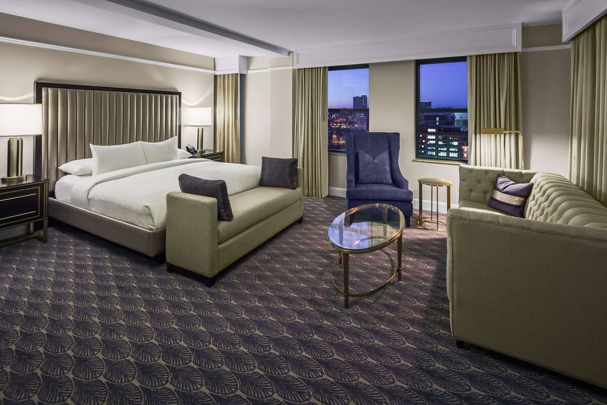 A hotel room with a bed, two armchairs, a small table, and a city view.
