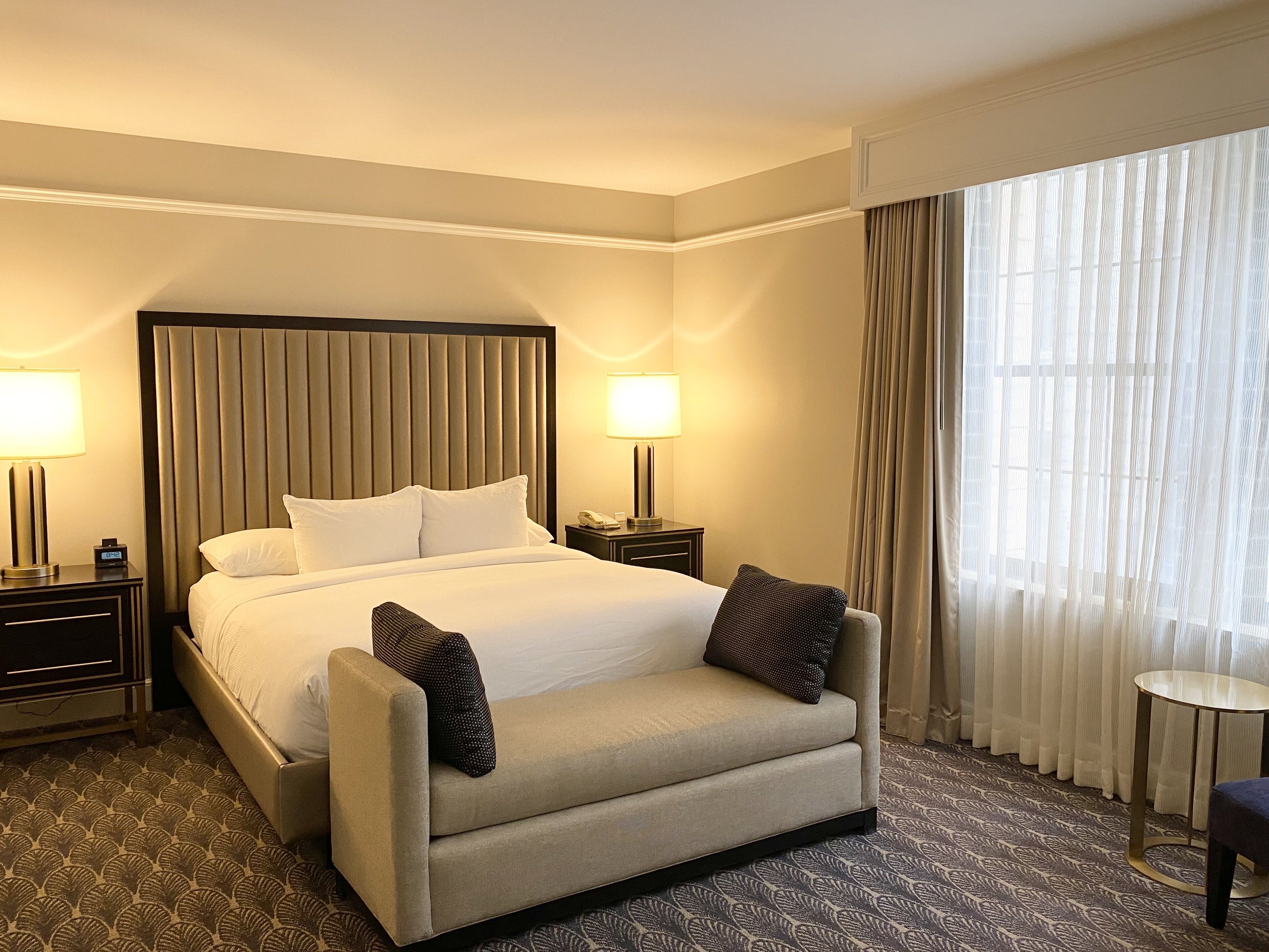 A hotel room with a large bed, two bedside tables, a small round table, and a chair.