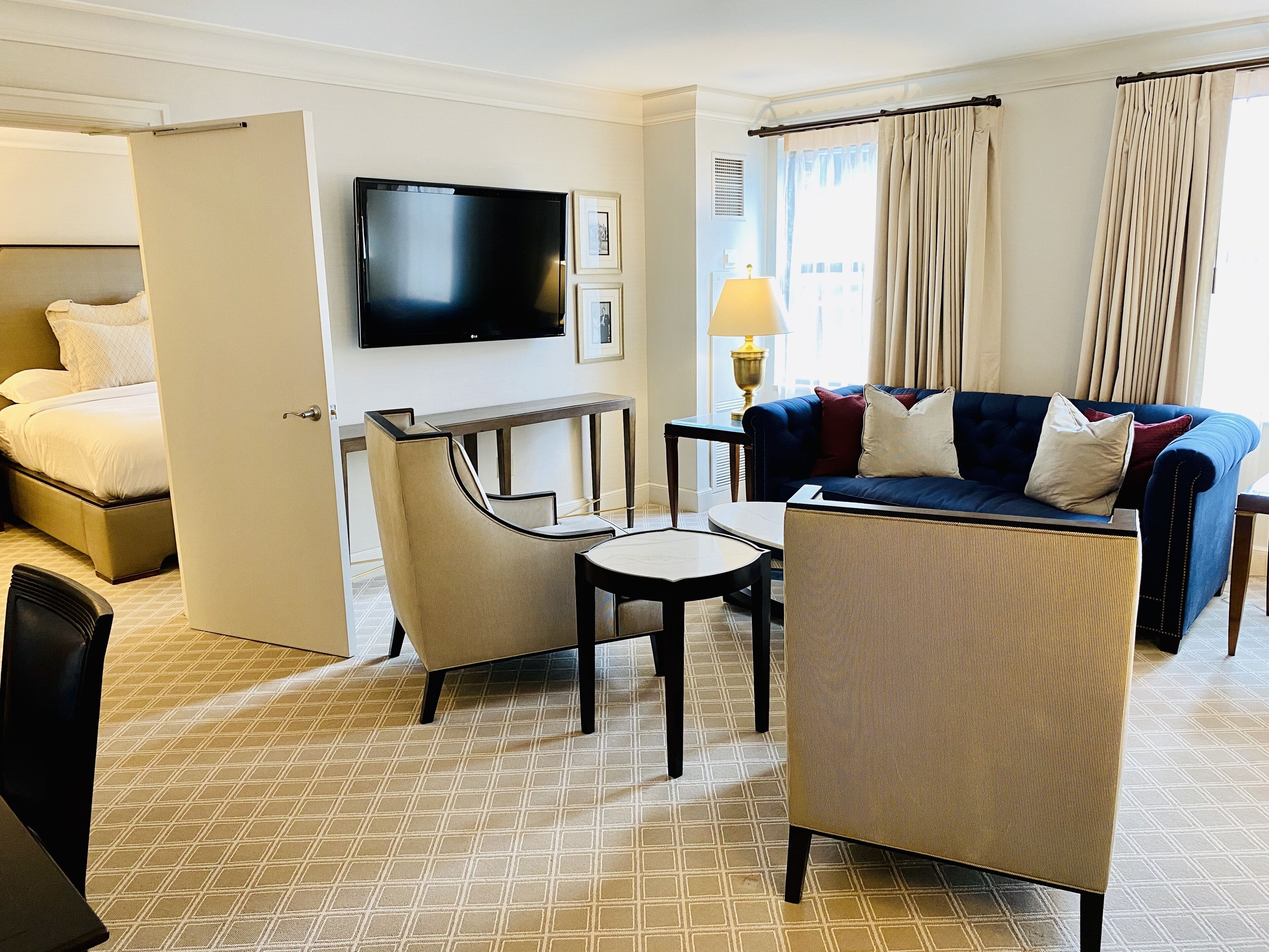 A hotel room with a bed, a TV, a sofa, a chair, a small table, and curtains.