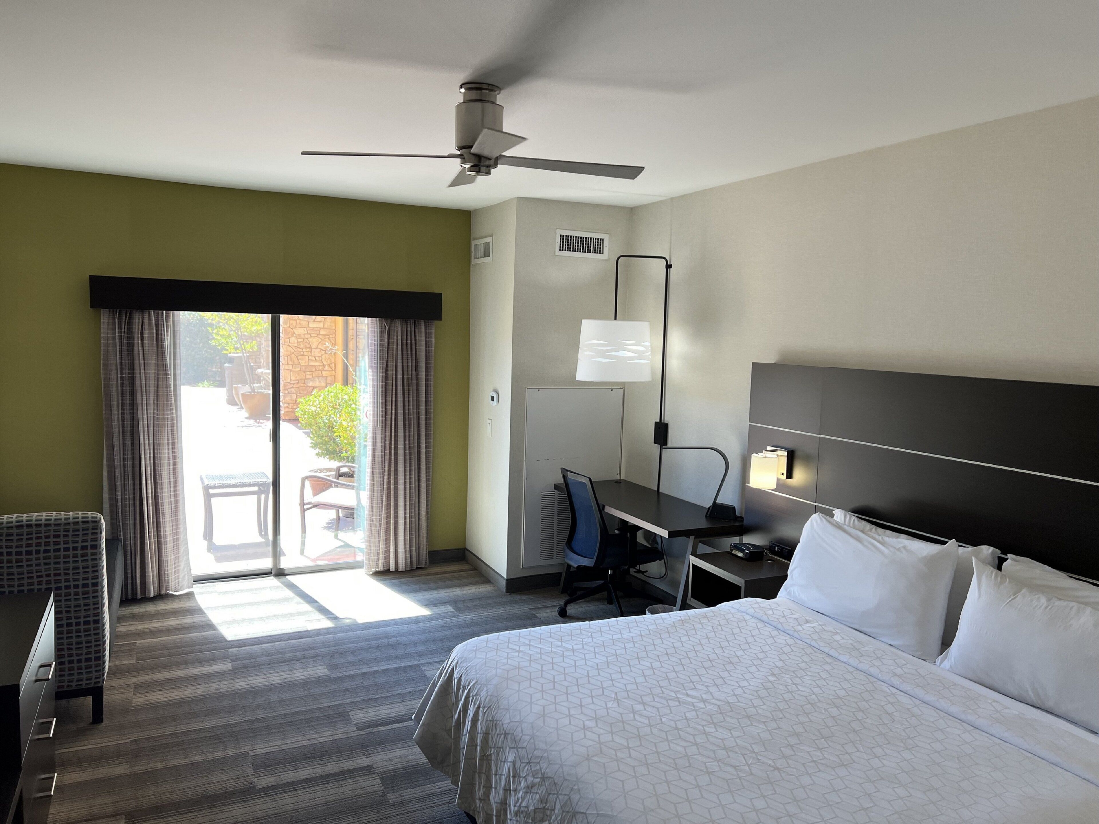Habitación de hotel con cama, escritorio, silla y ventilador de techo.