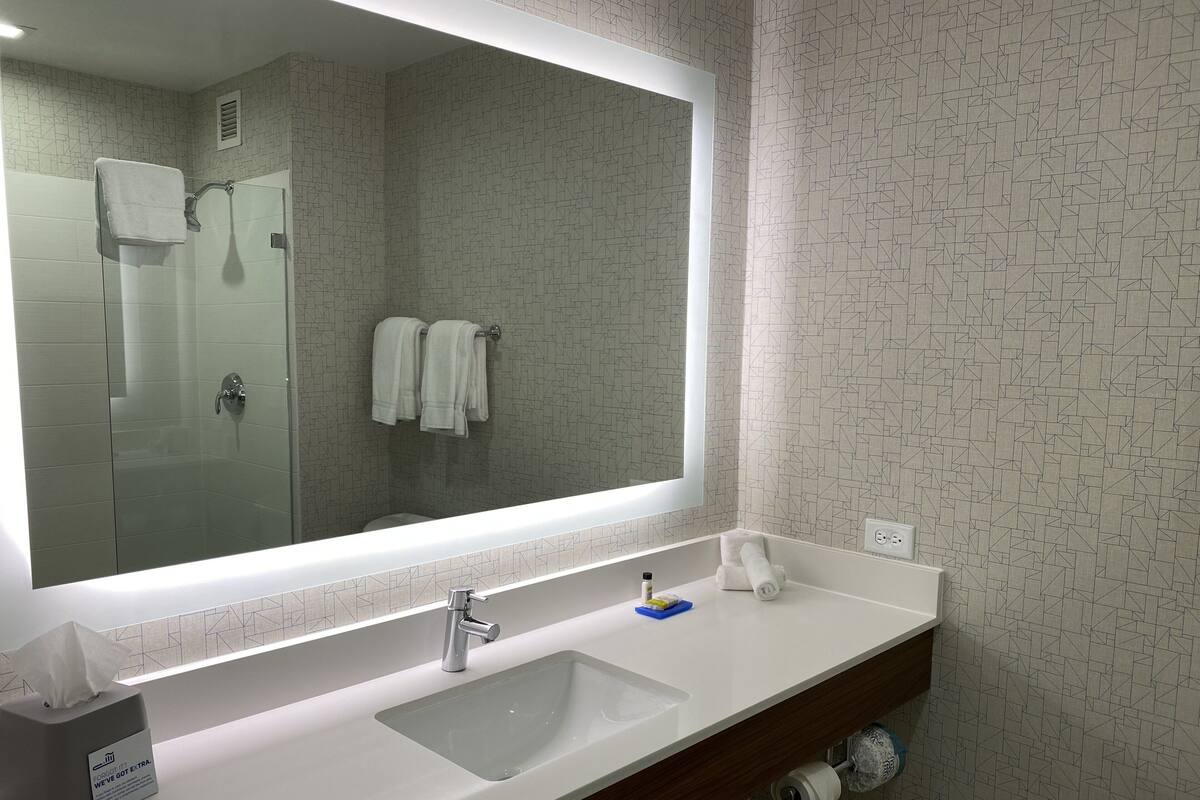 Une salle de bain avec un grand miroir, un lavabo blanc et une douche à parois de verre.