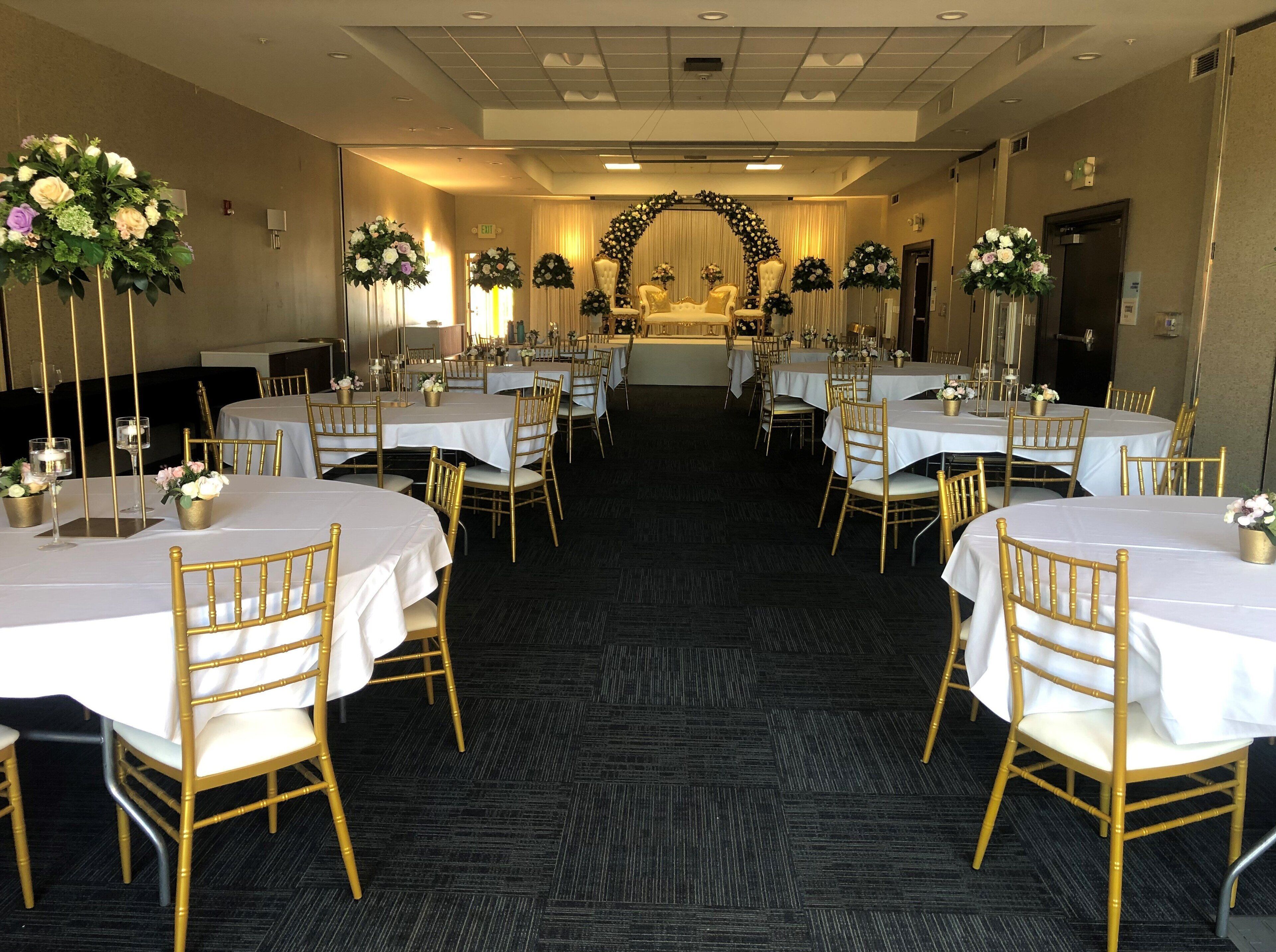 A banquet hall with round tables, gold chairs, and floral centerpieces.