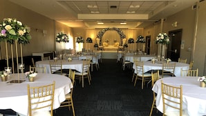 A banquet hall with round tables, gold chairs, and floral centerpieces.