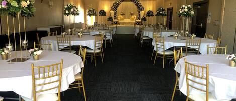 Une salle de banquet avec des tables rondes, des chaises dorées et des centres de table floraux.