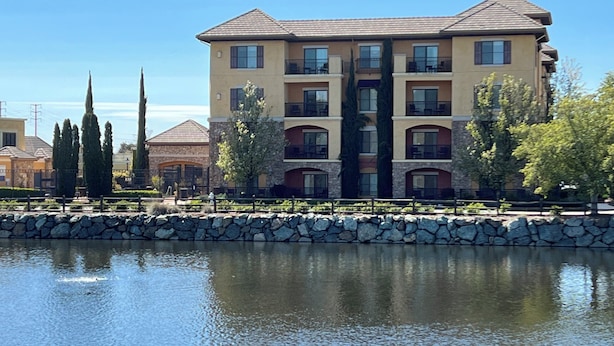 A multi-story hotel with a stone facade, multiple balconies, and a reflection in the water in front.