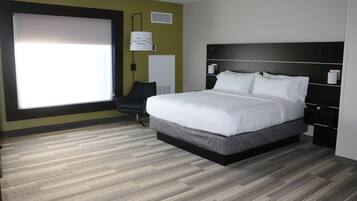 A modern hotel room with a large bed, a chair, a bedside table, and a window.