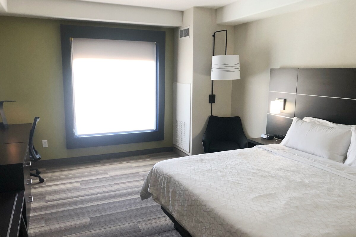 Een hotelkamer met een groot bed, een bureau met stoel, een raam met zonwering en een wandlamp.