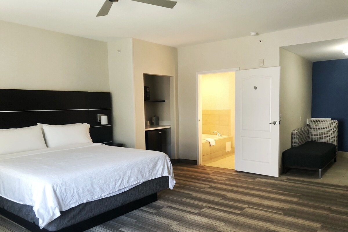 Een hotelkamer met een groot bed, een bureau, een stoel en een badkamer zichtbaar door een geopende deur.