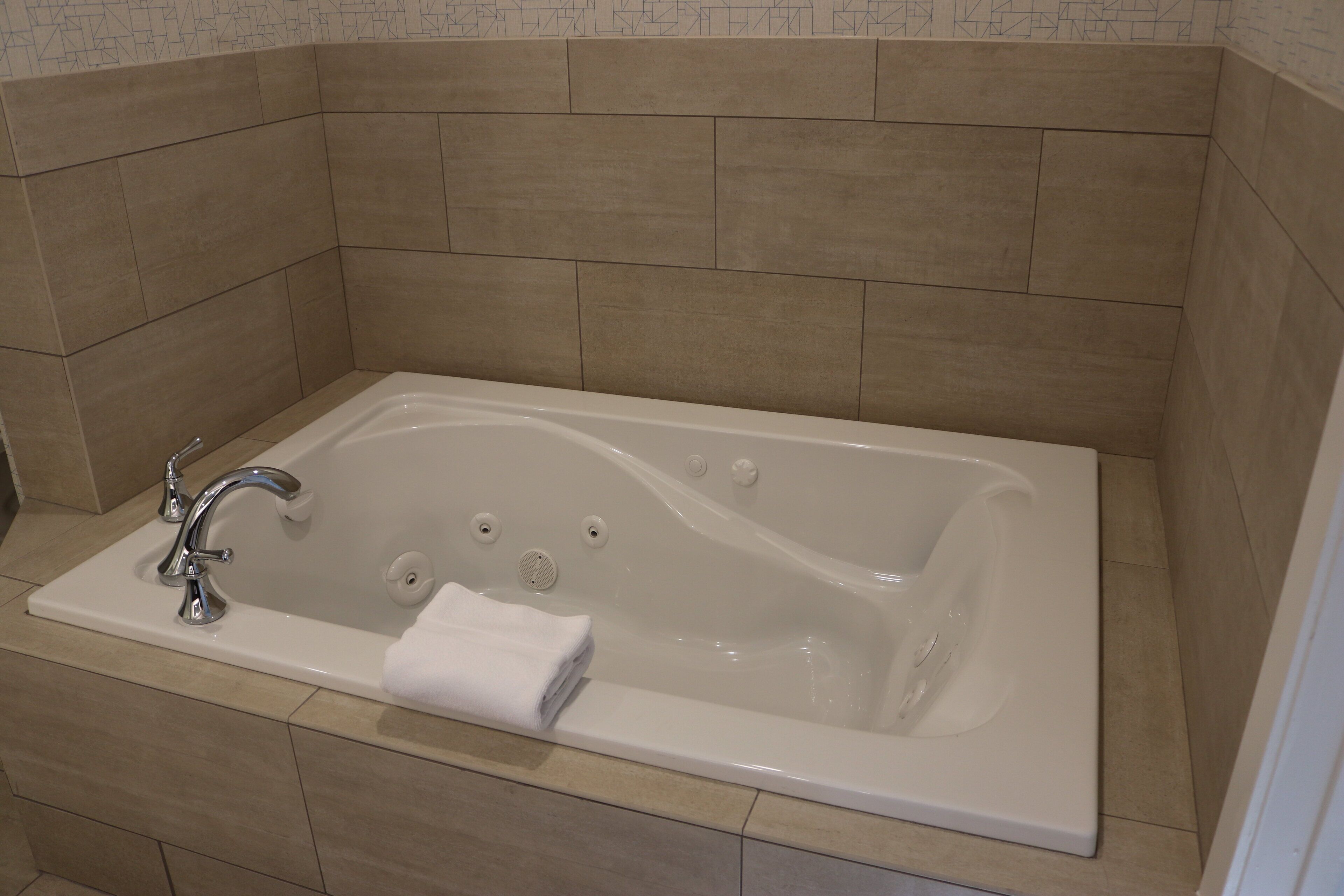 A modern bathroom with a rectangular bathtub, a single faucet, and a towel placed on the edge.