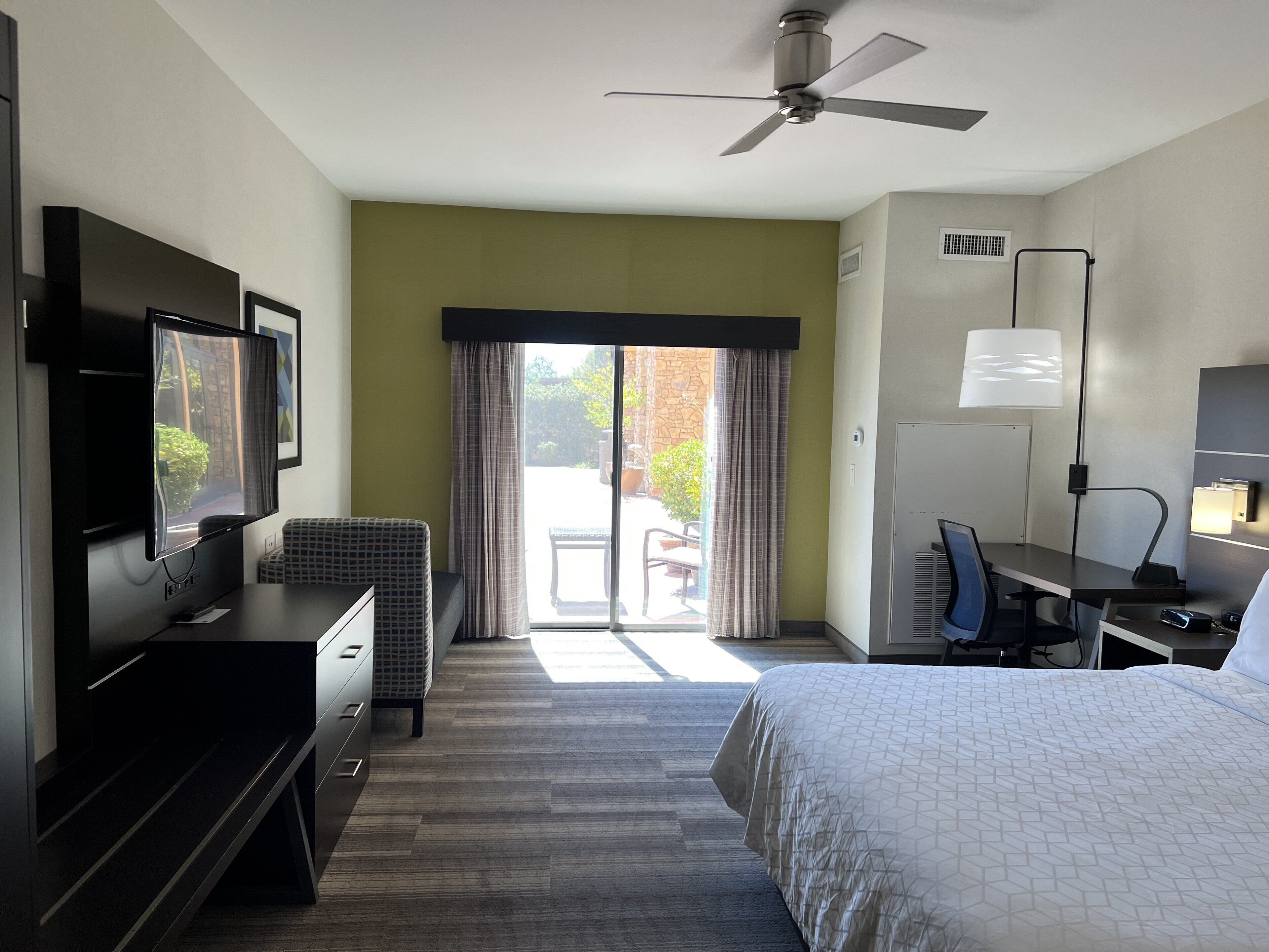 Une chambre d’hôtel équipée d’un lit, d’un bureau, d’une télévision et d’un ventilateur de plafond.