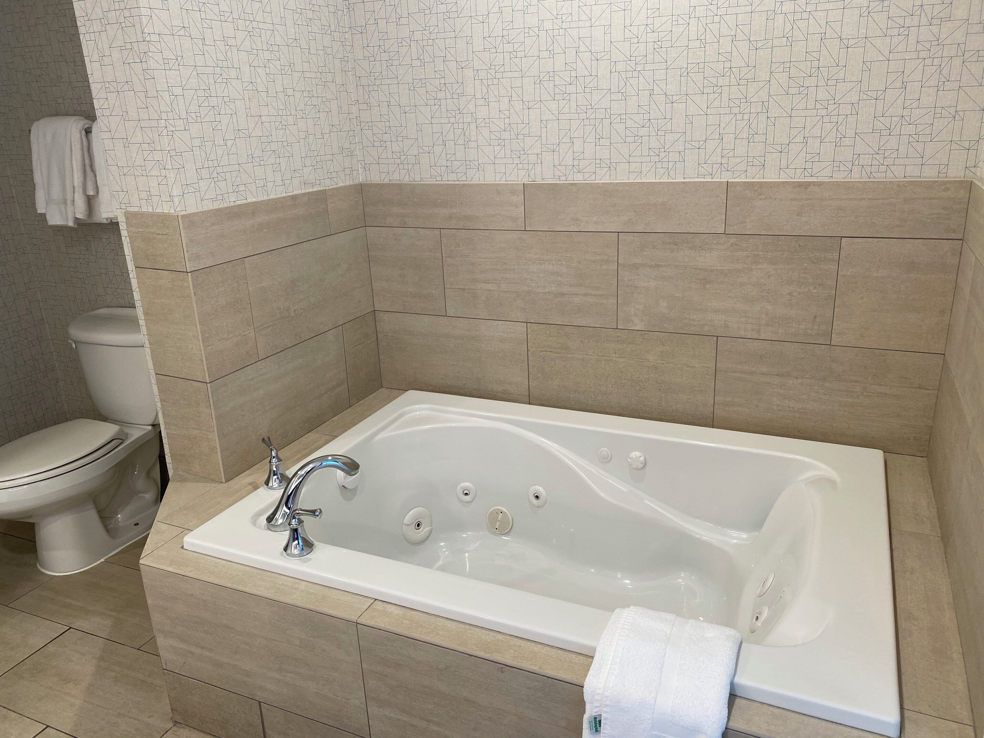 A bathroom with a bathtub, toilet, and tiled walls.