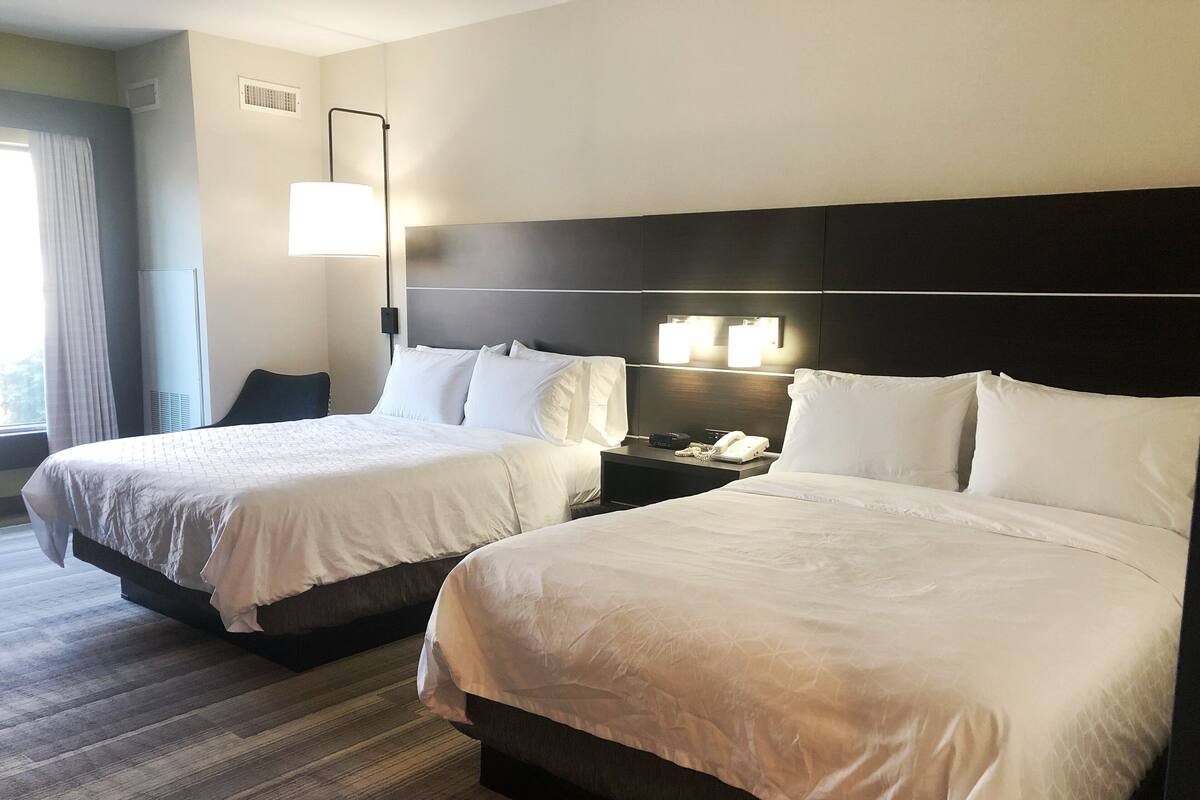Une chambre d’hôtel avec deux lits, une table de chevet avec un téléphone et une lampe, et une fenêtre avec des rideaux.