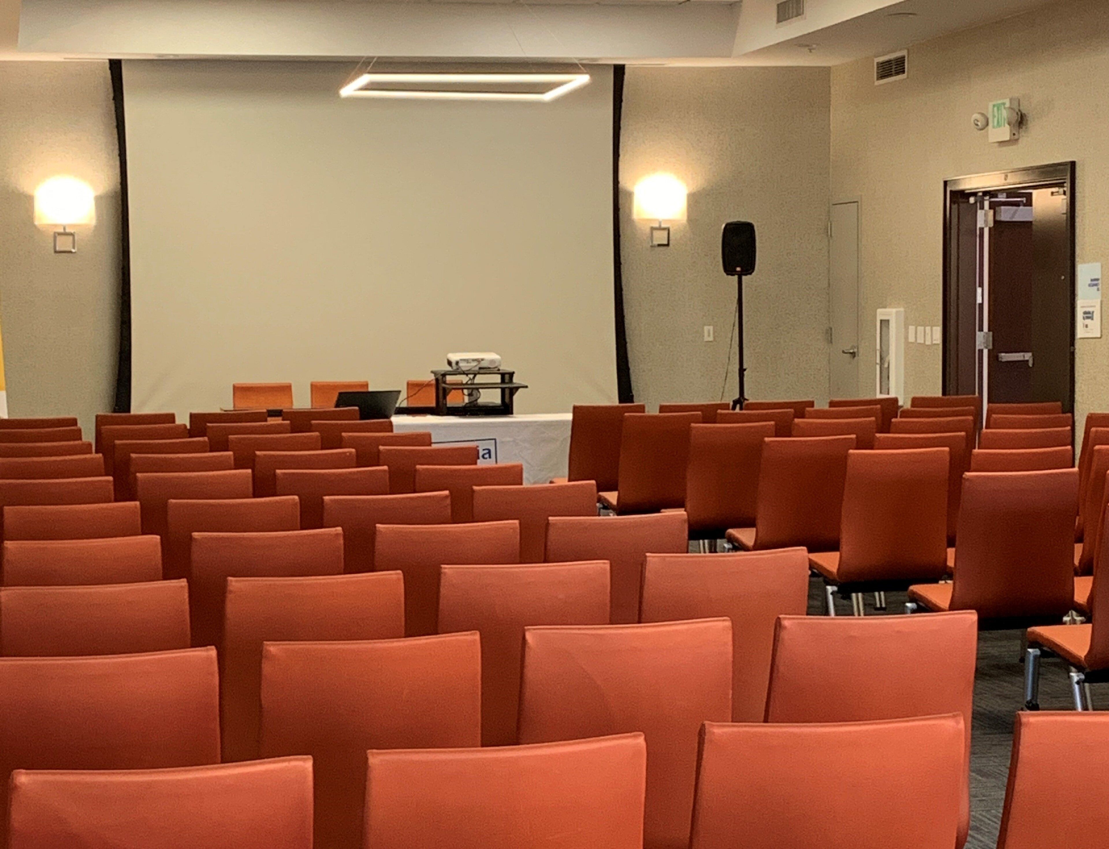 A conference room with rows of orange chairs, a projector, and a screen.