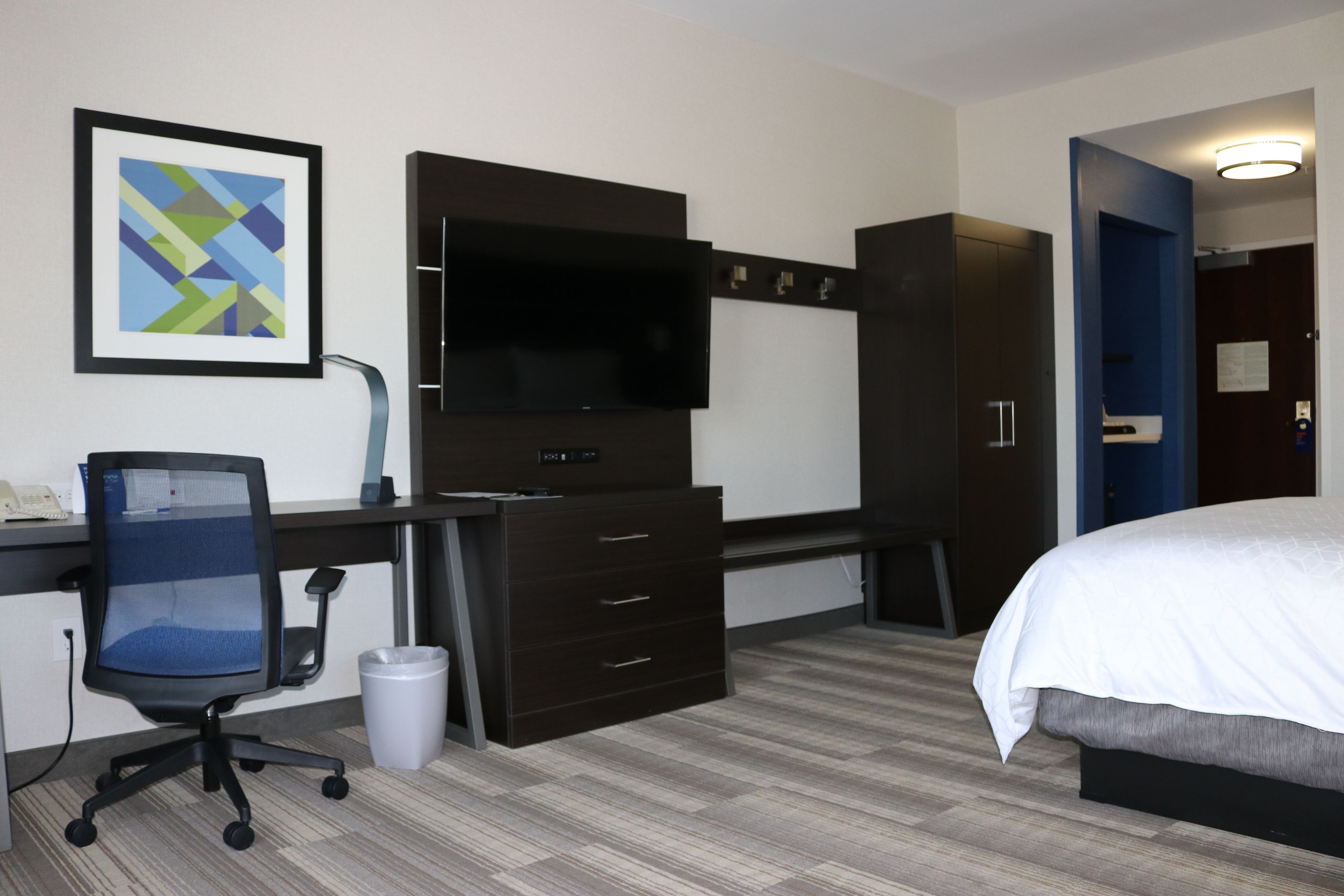Una habitación de hotel con cama, escritorio, computadora, televisor y cesto de basura.
