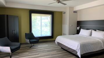 A hotel room with a bed, a chair, a wardrobe, a window, and a ceiling fan.