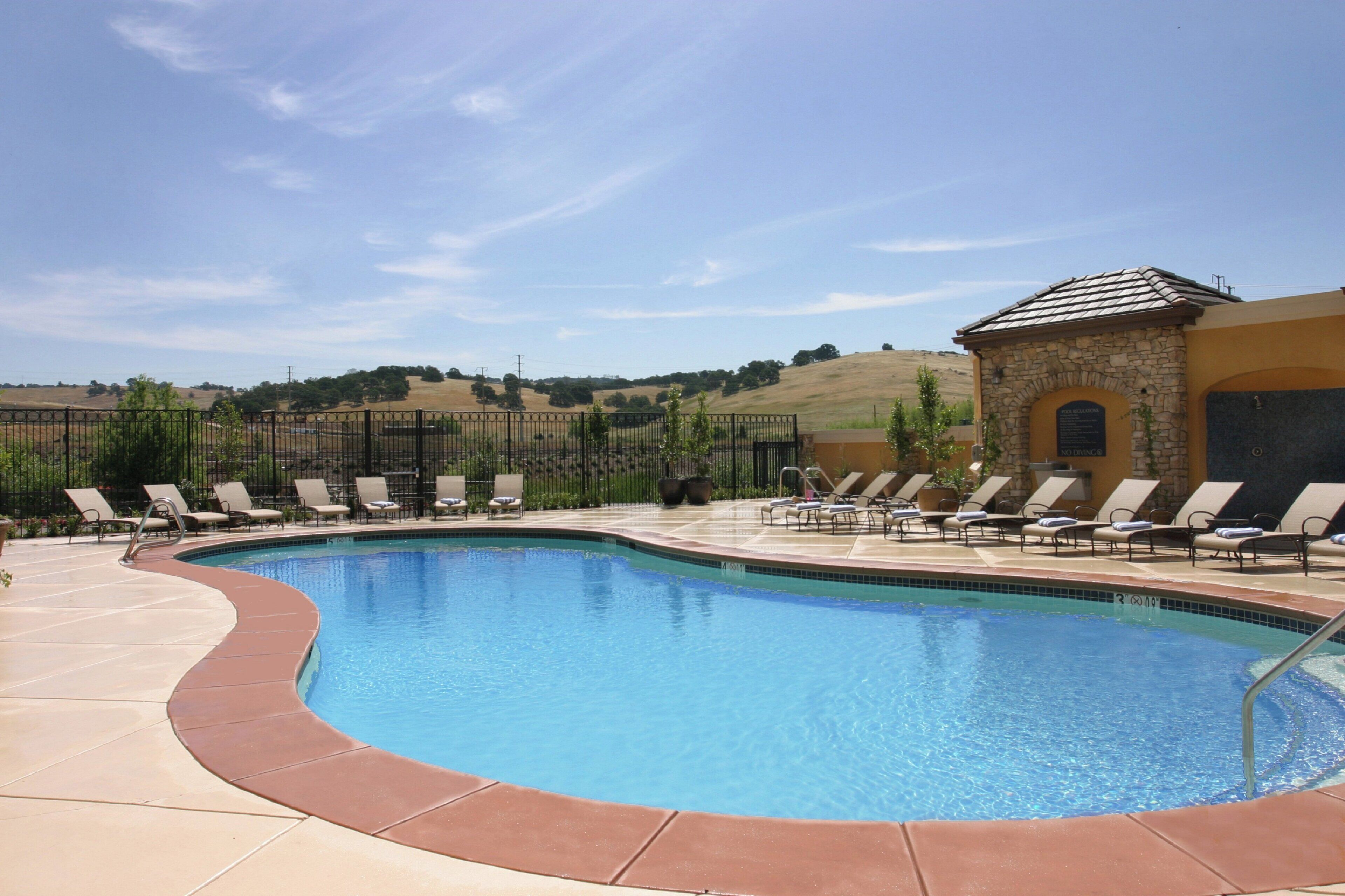 A swimming pool with lounge chairs and a stone building in the background.